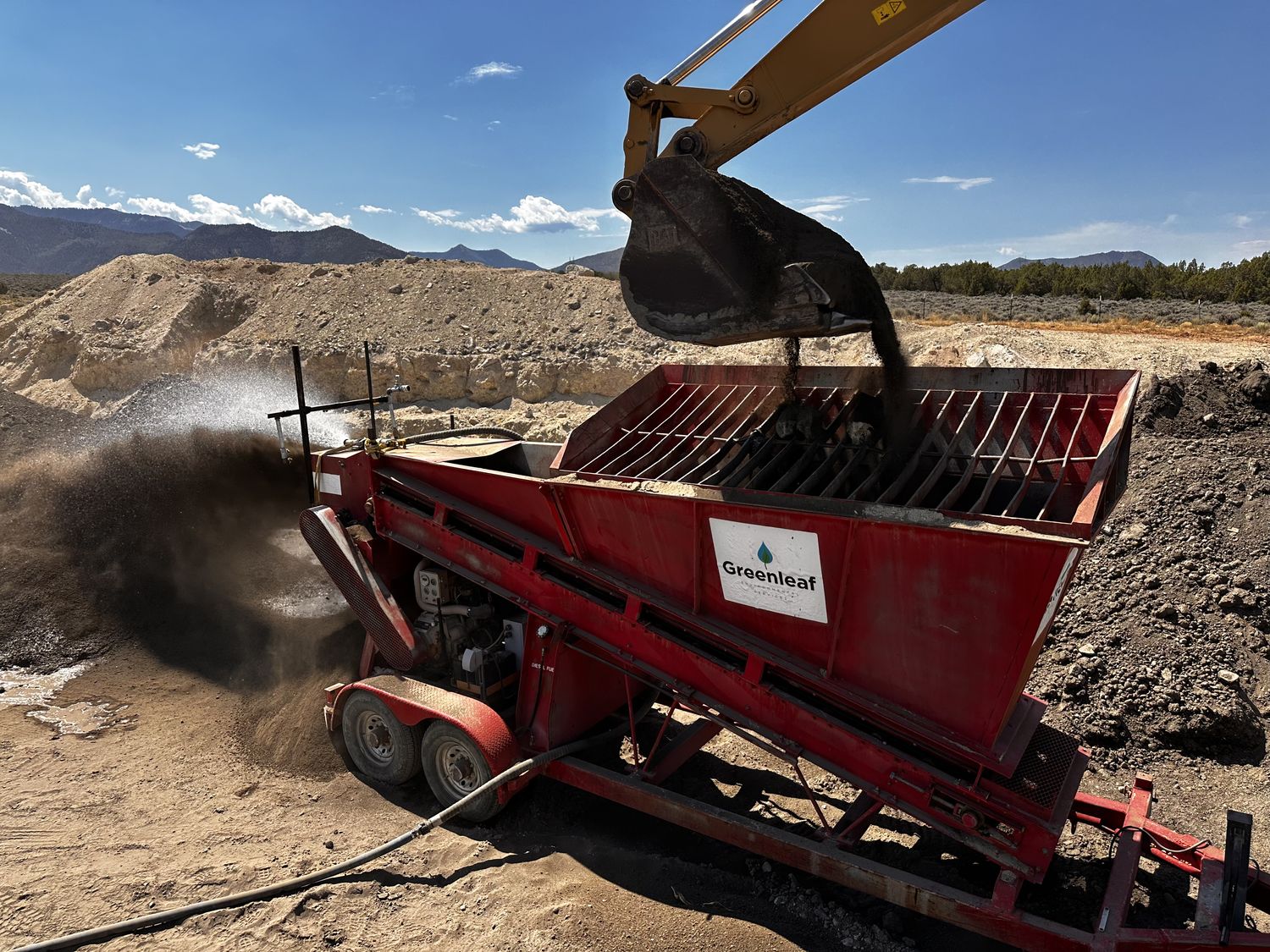 Excavator tipping impacted soil into a Greenleaf screening plant fitted with a dose spray bar